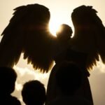 obraz, na którym możemy zobaczyć sylwetkę anioła obok kilkorga dzieci, których nie można zobaczyć wyraźnie ze względu na ciemność obrazu, w tle mamy niebo z chmurami i intensywne światło, które oświetla scenę w tle