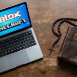 Obraz laptopa na stole z symbolami Roblox i Minecraft na ekranie; obok leży stara Biblia i różaniec.