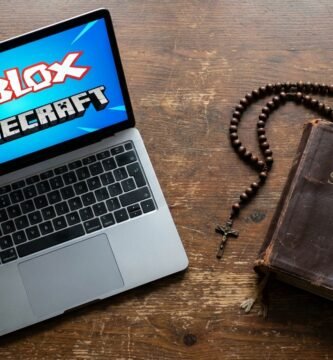 Obraz laptopa na stole z symbolami Roblox i Minecraft na ekranie; obok leży stara Biblia i różaniec.